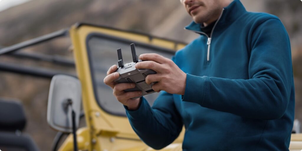 Person holding and operating a DJI RC 2 Remote Controller outdoors.