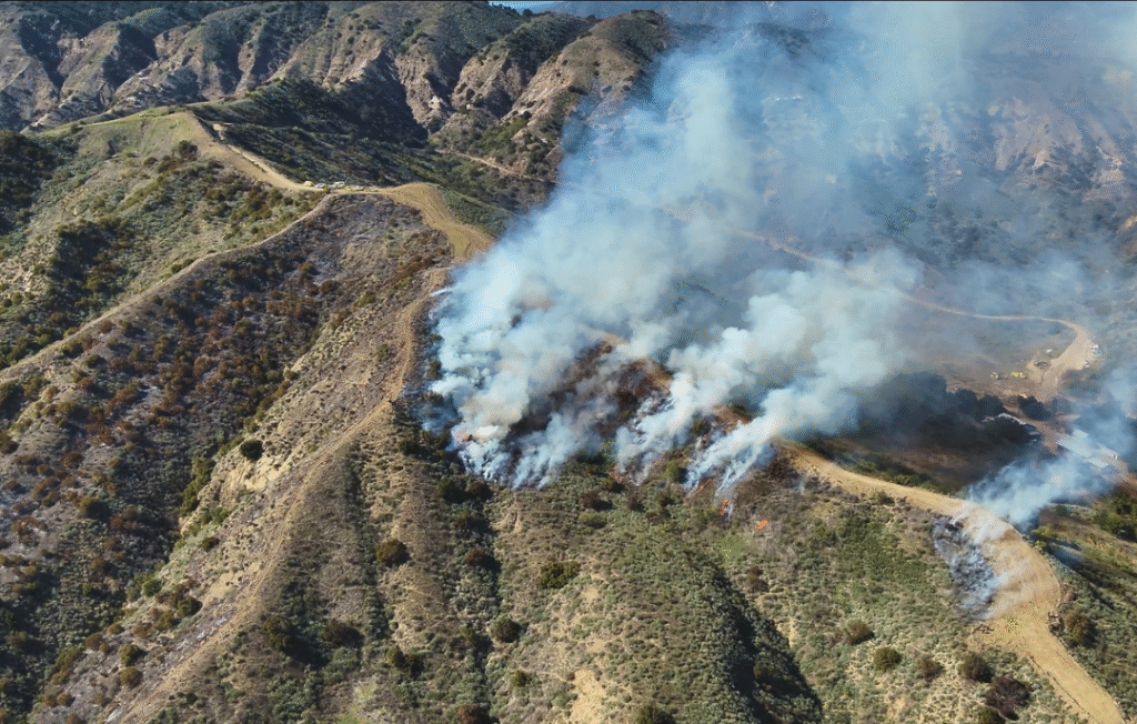 Wildfire drone response aircraft scanning a smoky fireline with thermal camera at sunset.